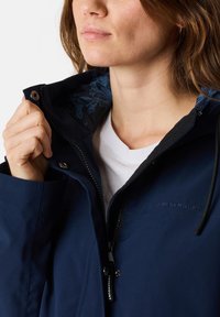 Navy blue waterproof jacket with a zip and snap closure, featuring a floral interior lining. Brand name "SWEDEMOUNT" embossed on chest.