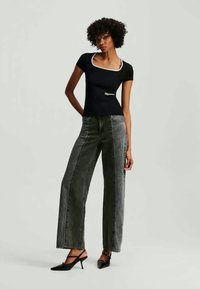 Čierny obtiahnutý tričko s bielym detailom na krku v kombinácii s šedými ďalekými nohavicami s vysokým pásom. Sada dopĺňajú jednoduché čierne lodičky.