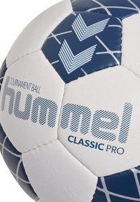 Vit och marinblå fotboll gjord av syntetiskt material, med hexagonala paneler, texturerad yta och tryckta logotyper och mönster.