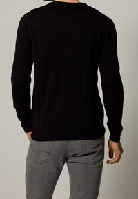 Maglione nero lavorato a maglia con maniche lunghe, collo tondo e orlo a coste. Indossato con jeans grigi, mostra una texture liscia e un design aderente.