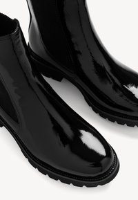 Černé Chelsea boty s lesklým povrchem, elastickými bočními panely a texturovanou gumovou podrážkou, s kulatou špičkou a kontrastním šitím.
