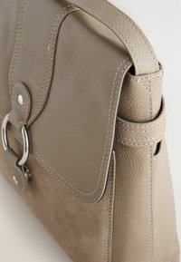 Beige lædertaske med en struktureret overflade, flaplukning, sølv hardware og kontrasterende syninger. Har en sidelukning.
