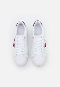 Weiße Ledersneaker mit glatter Textur, ausgestattet mit schwarzen und roten gestreiften Akzenten an den Seiten und Schnürsenkeln sowie einem Logo auf der Zunge.