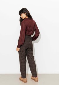 Blouse à manches longues bordeaux foncé avec col, associée à un pantalon à carreaux taille haute marron, présentant une jambe droite et des poches latérales.