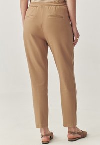 Pantaloni bej cu croială lejeră, talie elastică, două buzunare la spate și textură netedă. Combinat cu sandale maro, cu vârf deschis.