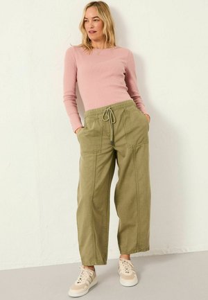 Grüne Baumwoll-Jogginghosen mit Seitentaschen und einem Bund mit Kordelzug, kombiniert mit einem figurbetonten pinken Langarmoberteil und beigen Sneakers.