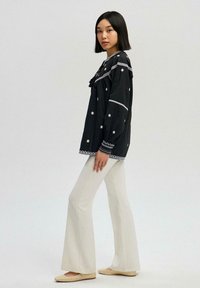 Black embroidered blouse with white floral patterns, bell sleeves, and a detailed neckline paired with cream flared pants and beige shoes.
