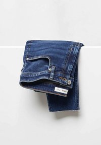 Jean bleu foncé plié avec poche et ceinture visibles, disposé sur une surface blanche devant un fond clair et uni.