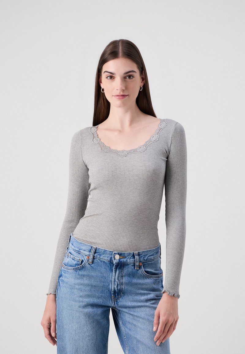 Grå ribbestrikket langermet topp med en bølgende blondekrage. Stoffet har en myk tekstur, kombinert med lyseblå høyprofilerte jeans.