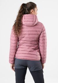 Rosa puffervinterjakke med hætte, prydet med et quiltet mønster og en tætsiddende pasform. Båret over mørke bukser, hvilket fremhæver en glat, let tekstur.