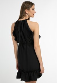 Schwarzes Kleid mit Rüschenschultern, gerafftem Taillenbereich und einem fransigen Saum mit Spitzenakzenten; gebundenes Rückendesign für eine verstellbare Passform.