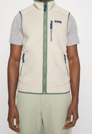 Creméfarbene Fleeceweste mit grünem Besatz und Reißverschlusstaschen, getragen über einem grauen Kurzarmhemd bei einer Person mit dunkler Haut.