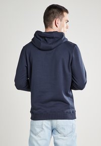 Sudadera con capucha de color azul marino hecha de un tejido suave. Cuenta con una capucha ajustable con cordones y puños y dobladillo de canalé. Diseño liso sin logotipos visibles.