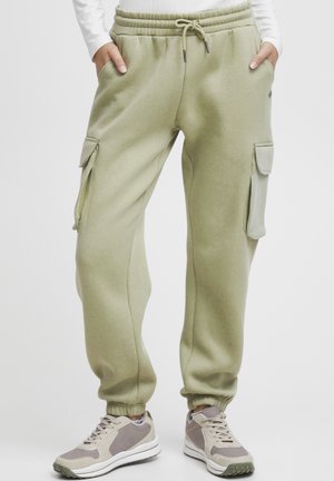 Green sweatpants with a drawstring waist, side pockets, and cargo-style patch pockets; made from soft, textured fabric with ribbed cuffs.