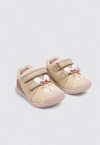 Scarpe beige per bambini con una finitura scintillante, caratterizzate da un design a forma di faccia di coniglio e un fiocco rosa, fissate con due strap in Velcro su una suola in gomma.