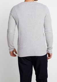 Grå långärmad stickad tröja med texturerad tyg, rund halsringning och rak nederkant. Bärs med mörka randiga byxor.