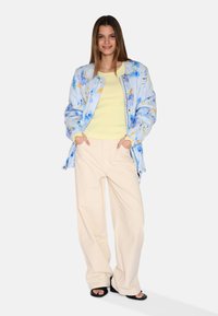 Svetlomodrá bomber bunda s kvetinovým vzorom, žltý rebrovaný top a krémové široké nohavice. Čierne šľapky dotvárajú outfit.