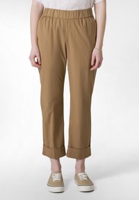 Brązowe, lekkie spodnie z elastycznym pasem, o długości 3/4 i podwiniętych mankietach. W zestawieniu z beżowymi sneakersami, tworzą casualowy look.