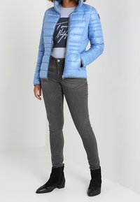 Helle blaue Puffjacke mit einem Reißverschluss und Stehkragen, kombiniert mit grauen Skinny-Jeans und schwarzen Knöchelstiefeln.