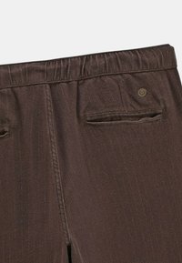Pantalons bruns avec taille élastique, dotés de deux poches arrière et de délicates rayures verticales sur une texture lisse.