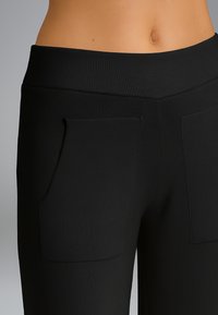 Pantaloni neri a coste con una vita alta e due tasche frontali. Il tessuto ha una texture liscia e un design aderente.