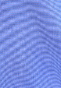 Zbliżenie niebieskiej tkaniny o drobnym, fakturowanym splocie ukazującym zmiany światła i cienia.