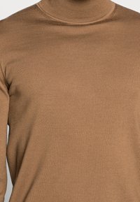 Brun ribbad höghalssweater med en åtsittande passform. Texturen är mjuk och len, med en hög krage och långa ärmar.