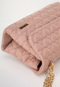 Růžová prošívaná kožená kabelka se zlatým řetízkovým popruhem, se srdíčkovým vzorem a prošívanými detaily na vnějším povrchu.