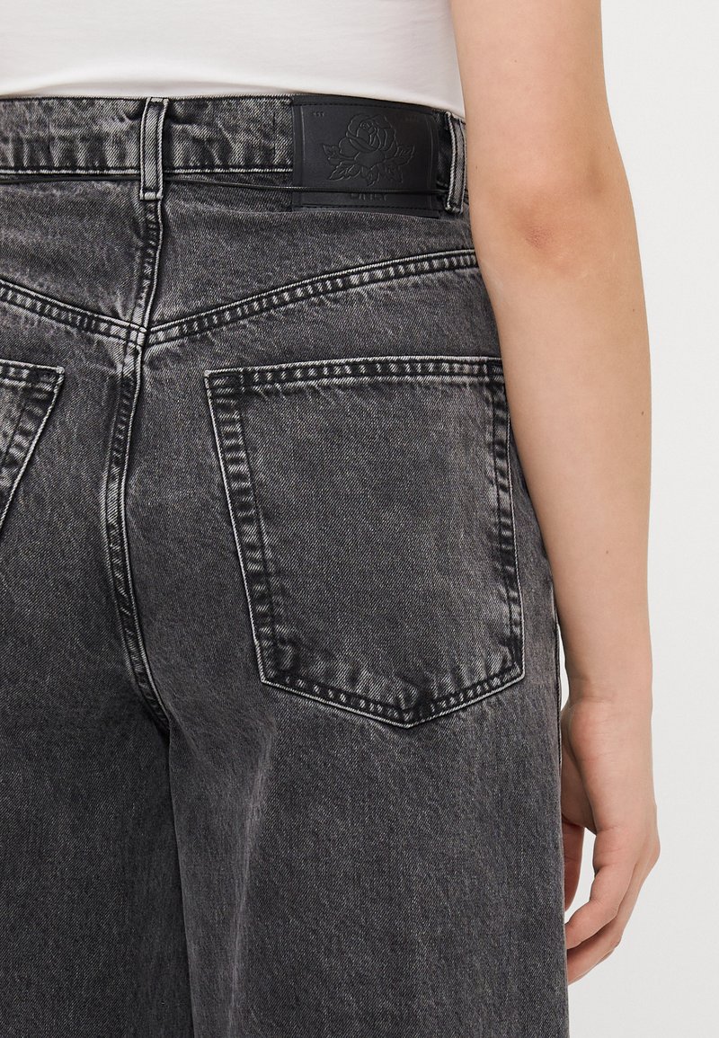 Jeans in denim nero con una finitura sbiadita, con vita alta, due tasche posteriori e un'etichetta in pelle nera testurizzata in vita con un design floreale.