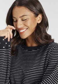 Black and white striped sweater with a soft texture, featuring small heart patterns on the sleeves and a classic round neckline.