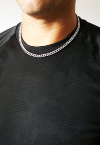 Collana in argento indossata da una persona con una maglietta nera a trama, caratterizzata da anelli spessi e una superficie liscia.