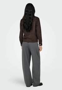 Camisa de ante marrón de manga larga con puños abotonados, combinada con pantalones grises de corte holgado. Textura suave, con un mínimo de detalles.