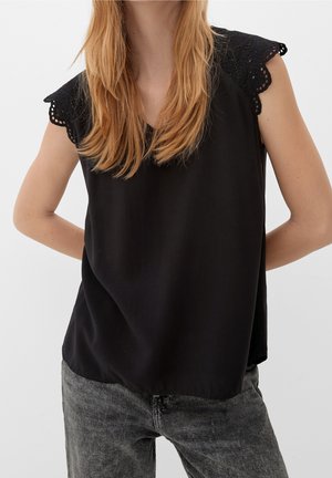 Zwarte mouwloze top met geschulpte kanten details op de schouders, zachte stof, V-hals ontwerp, gecombineerd met grijze jeans. Eenvoudige en moderne snit.