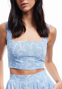 Blauwe gestreepte crop top met witte bloemendetails, vierkante halslijn en brede bandjes. De stof heeft een soepele textuur met een aansluitend ontwerp.