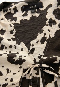 Black and white cow print wrap shirt with a v-neckline, soft texture, and a fabric tie at the waist, featuring contrasting diagonal seams.