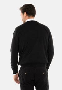 Maglione nero a maglia con una texture a coste, scollatura rotonda e vita aderente, abbinato a pantaloni scuri con doppi tasconi posteriori.