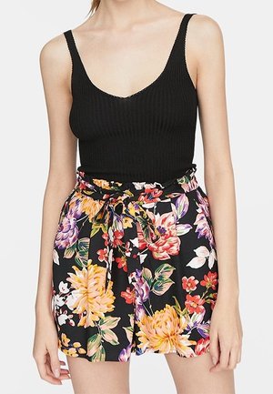 Débardeur noir côtelé associé à un short à fleurs taille haute aux couleurs vives, avec une ceinture à nouer et un tissu léger et doux.