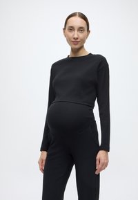 Top de maternidade preto canelado com mangas compridas e decote redondo, combinado com calças pretas caneladas correspondentes, ajustadas na cintura e nos quadris.