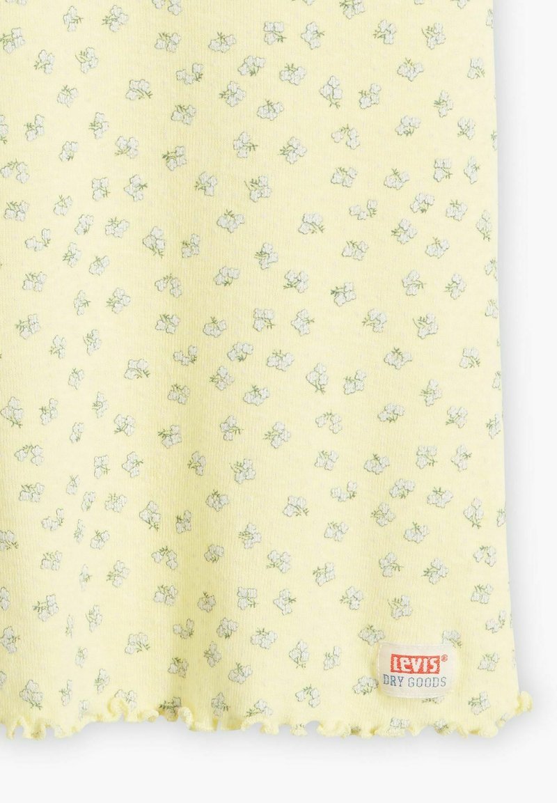 Tela amarilla con pequeño patrón floral blanco y dobladillo scalloped, presentando una etiqueta de Levi's Dry Goods en el borde inferior.