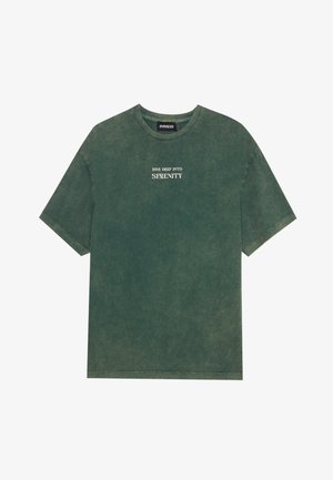 T-shirt in cotone verde con scollatura rotonda e maniche corte. Presenta una stampa sbiadita della scritta "DIVE DEEP INTO SERENITY" in bianco. Texture morbida.