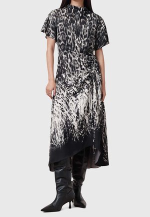 Czarna i biała sukienka w nadruk z krótkimi rękawami, marszczonym szczegółem po boku oraz asymetrycznym dołem. Połączona z czarnymi kozakami za kolano.