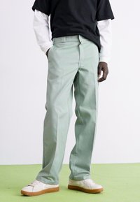 Light green straight-leg trousers made of cotton blend, featuring side pockets and a smooth texture, worn with a black and white layered top.