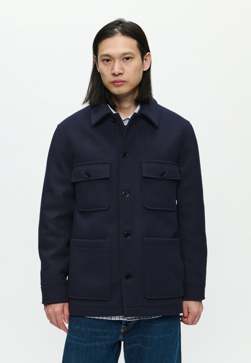 Navy wool blend jacket with a structured shape, featuring a collared neckline, four front pockets, and button closure.