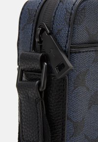 Borsa a tracolla in pelle nera e tessuto blu a motivo con una zip prominente e hardware con cinturino regolabile. Accenti testurizzati visibili.