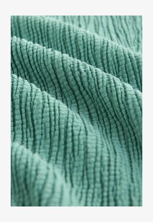 Tejido texturizado en suave color verde menta, con profundas estrías verticales y una apariencia esponjosa, que transmite una sensación acogedora y atractiva.