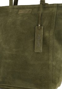 Olivegrüne Wildleder-Totetasche mit strukturierter Oberfläche, ausgestattet mit einem Markenetikett. Weiches Material und rechteckige Form mit doppelten Griffen.