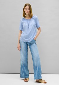 Blusa a righe blu chiaro con maniche corte, scollatura arricciata, abbinata a jeans in denim chiaro a gamba larga e sandali color cammello. Design semplice.