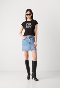 Schwarzes, kurzes T-Shirt mit silbernem "DK NY"-Logo, kombiniert mit einem hellblauen Denim-Minirock und knielangen schwarzen High Heels.
