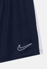Pantalones cortos deportivos azul marino oscuro con un panel lateral blanco y un pequeño logo blanco de Nike en el dobladillo. Tela suave con una textura ligera.