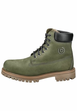 Botín de tobillo de ante verde con detalles en cuero negro, cuello acolchado y ojales metálicos. Presenta una suela de goma texturizada y detalle de logo.